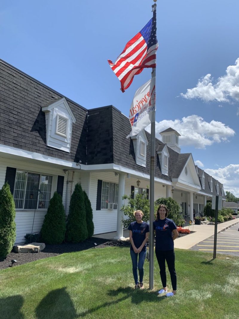 2 Intrex employees and the American flag outside of a senior living community